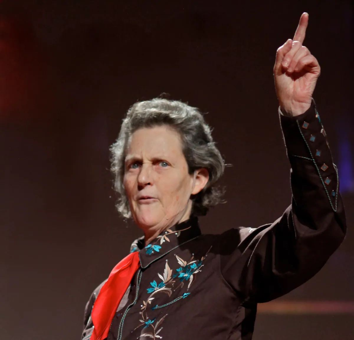 Temple Grandin speaking at TED in 2010 with one arm raised.